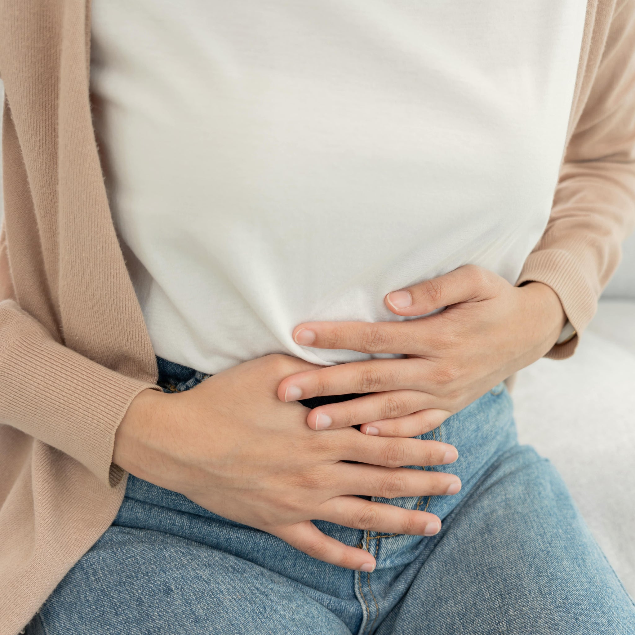 Eine Frau hält sich den Unterbauch, um Unwohlsein und Beschwerden im Intimbereich anzudeuten