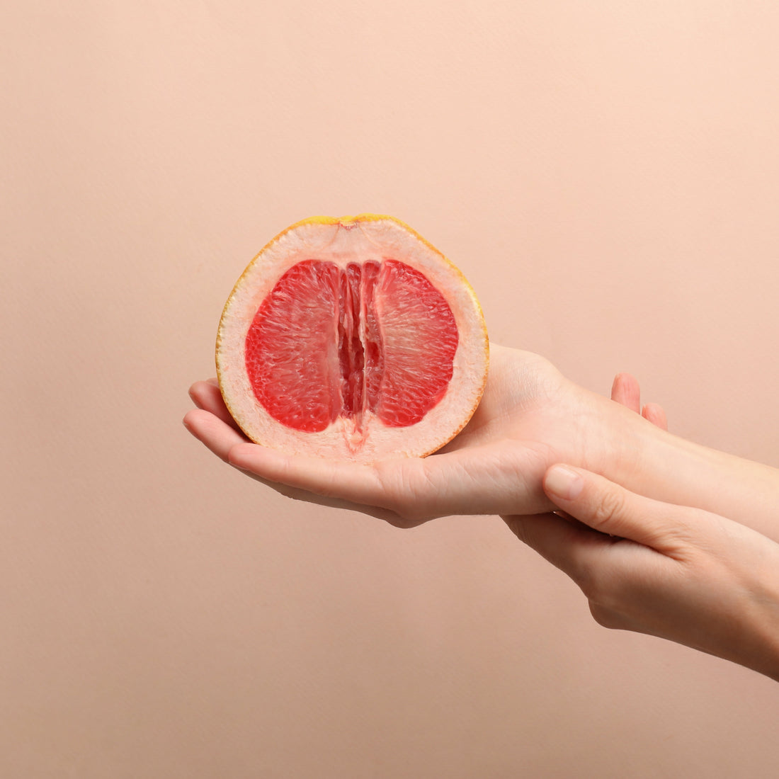Frau hält eine halbe Grapefruit, die eine Vagina repräsentieren soll